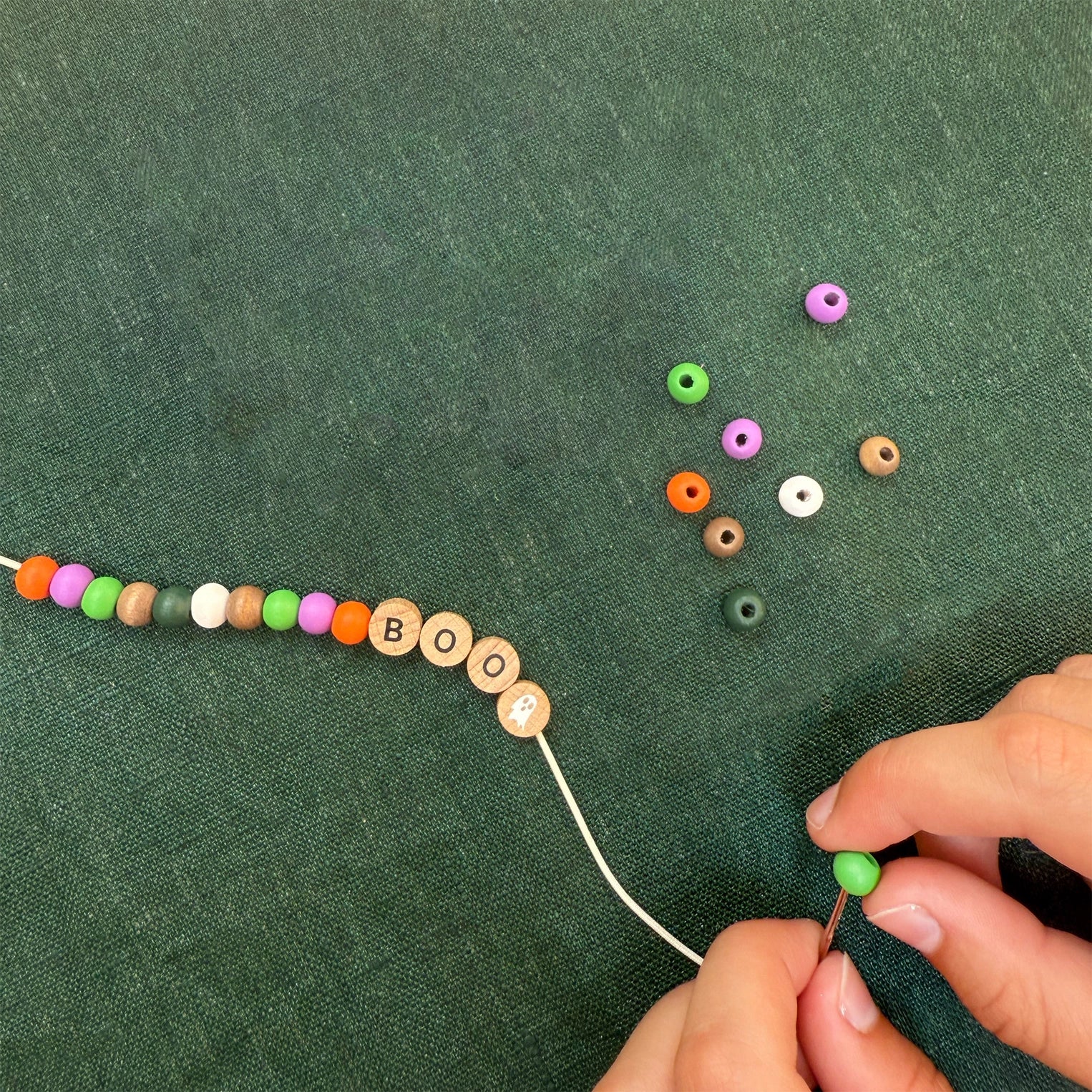 Person stringing colorful beads on a green fabric background