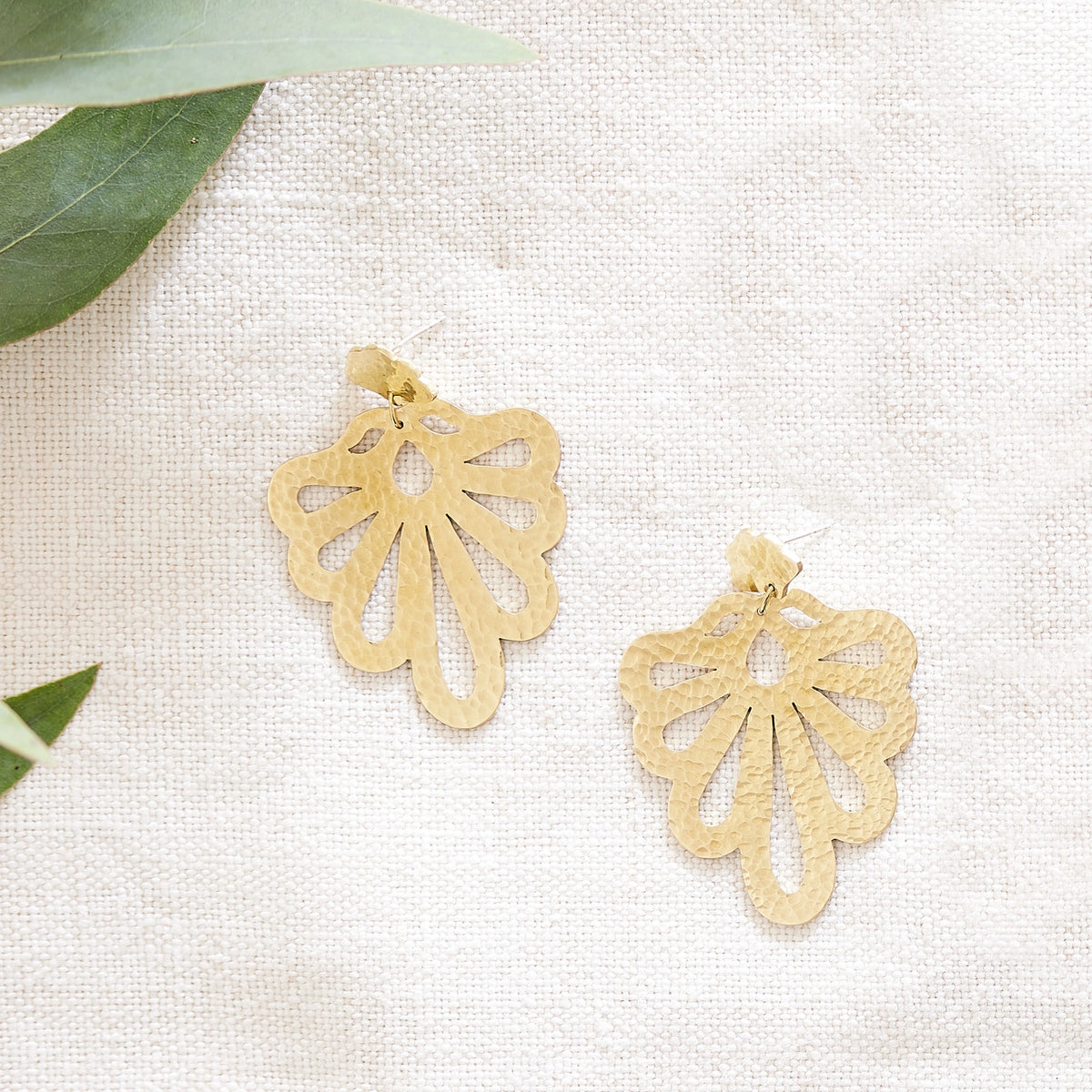 Hammered peacock statement studs on a hessian background with green leaves.