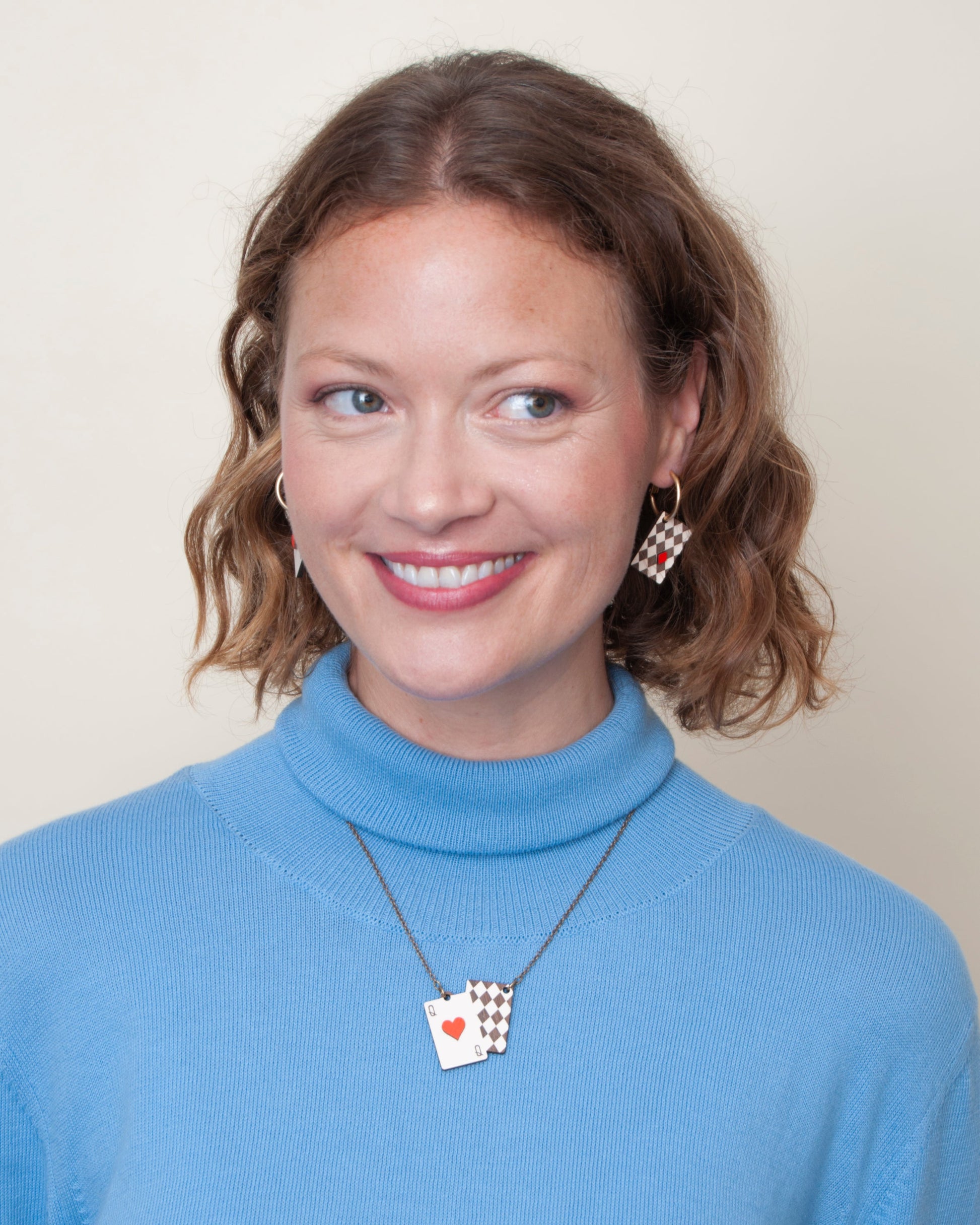 Woman wearing a blue turtleneck sweater with a necklace featuring a card pendant.
