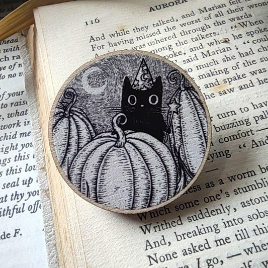 Wooden badge with black cat and pumpkin design on an open book
