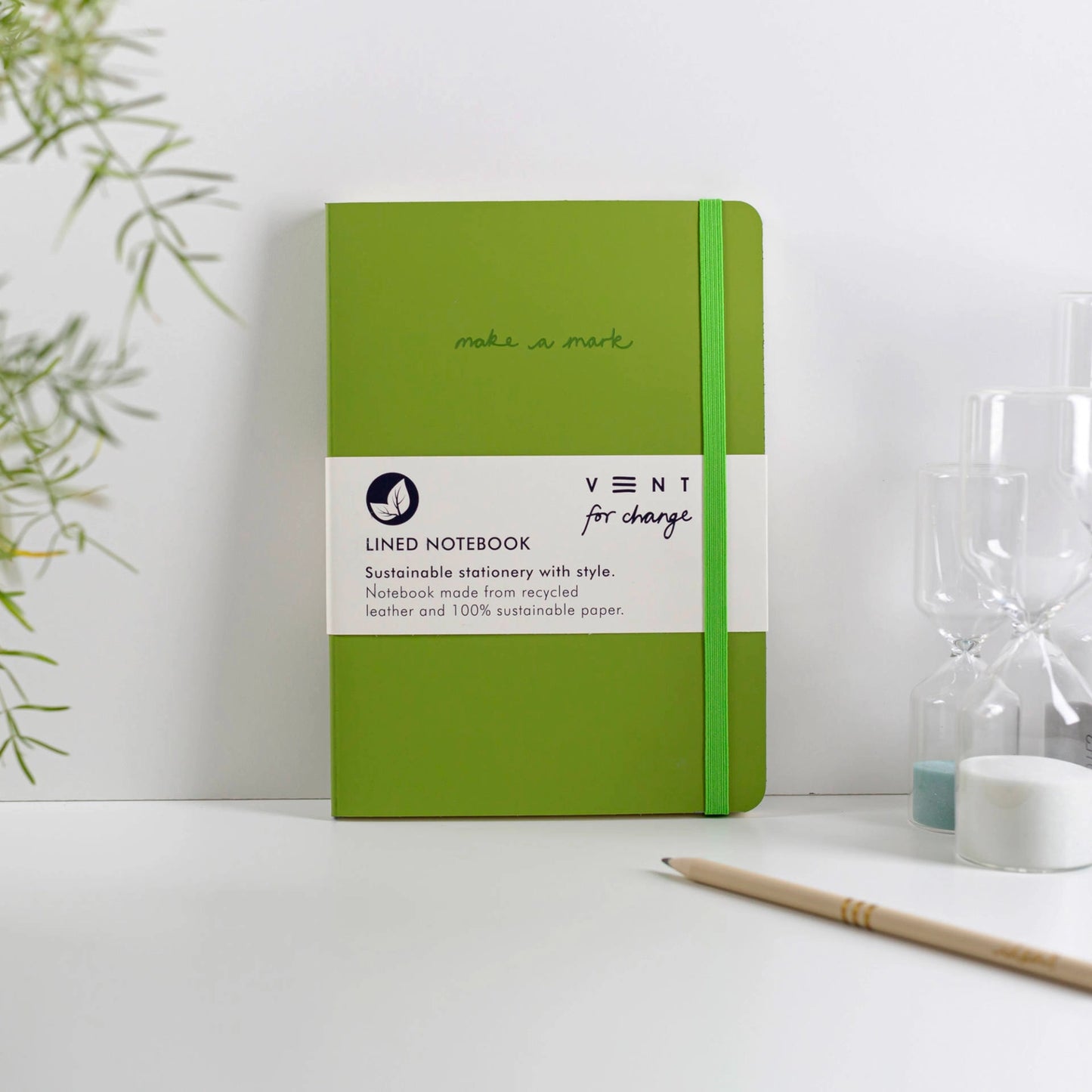 Green notebook with a label on a white surface with a plant in the background