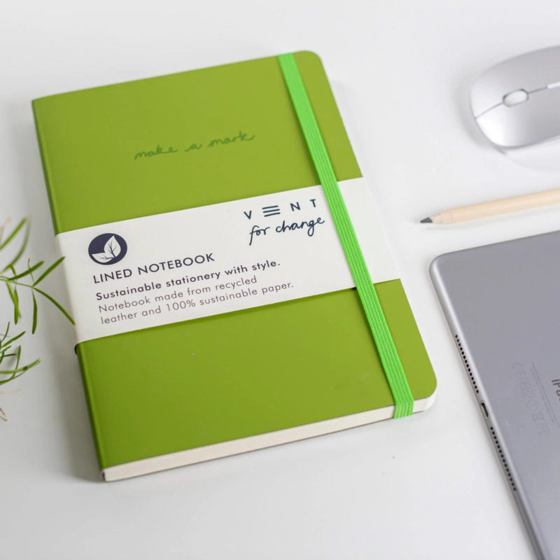 Green notebook with a label on a white surface with office items.