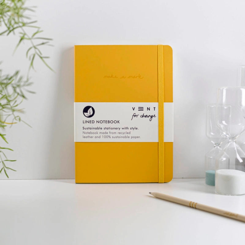Yellow notebook with a label on a white surface with a plant and hourglass in the background