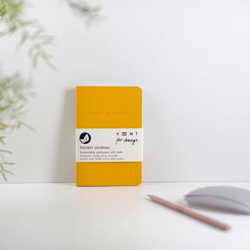 Yellow pocket journal with a white label on a light surface with a plant in the background