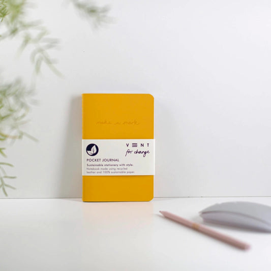 Yellow pocket journal with a white label on a light surface with a plant in the background