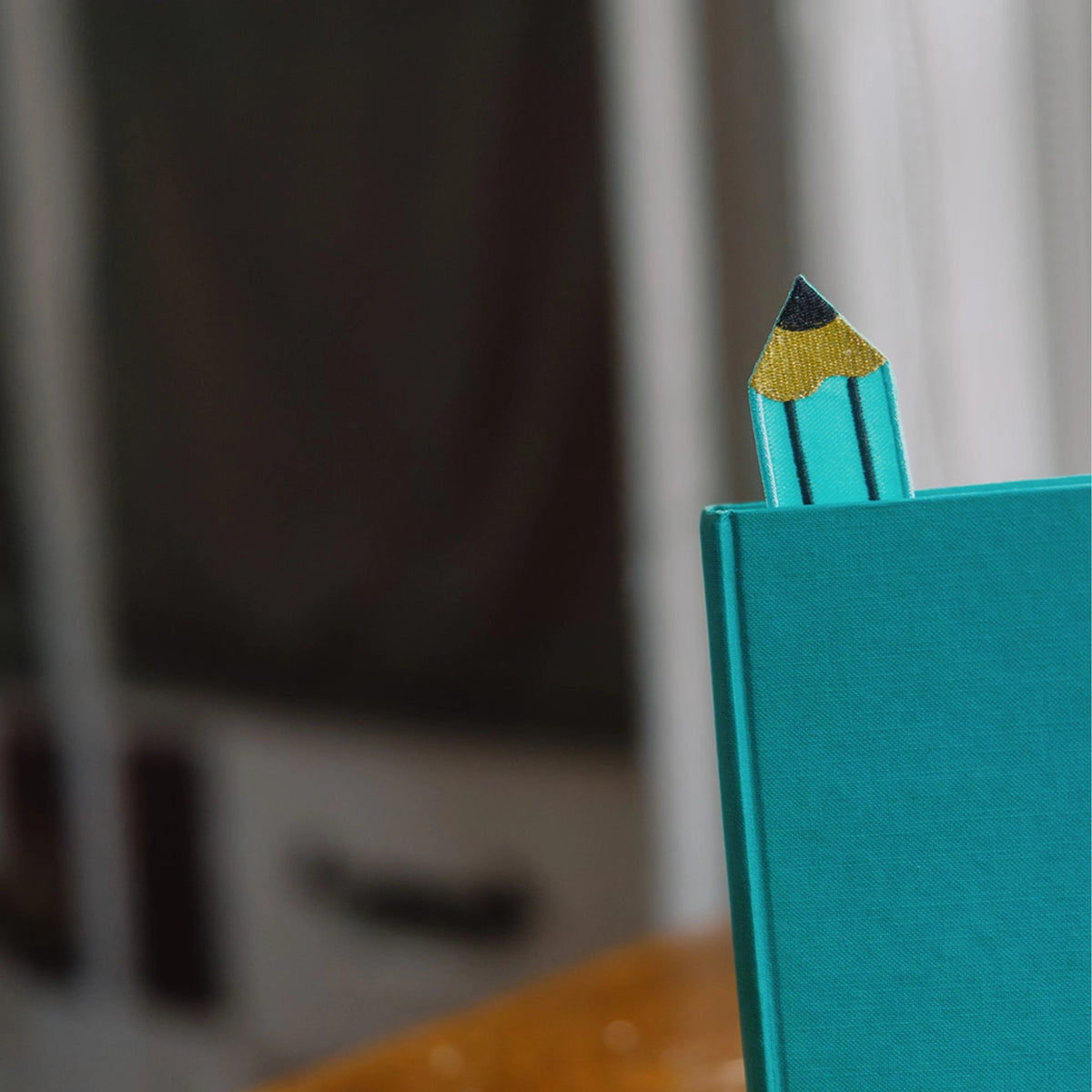 Teal notebook with a decorative pencil on top against a blurred background