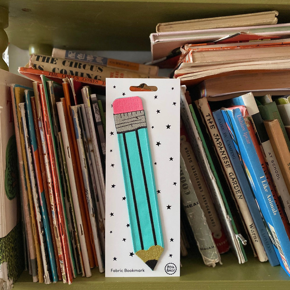 Fabric bookmark packaging with a pencil design on a bookshelf background