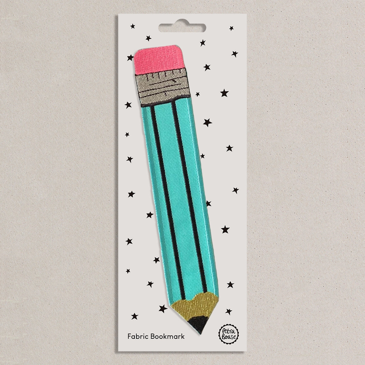 A fabric bookmark shaped like a pencil, attached to a white backing card with black star prints. The pencil is turquoise with black lines, a pink eraser, a gray ferrule, and a gold tip.