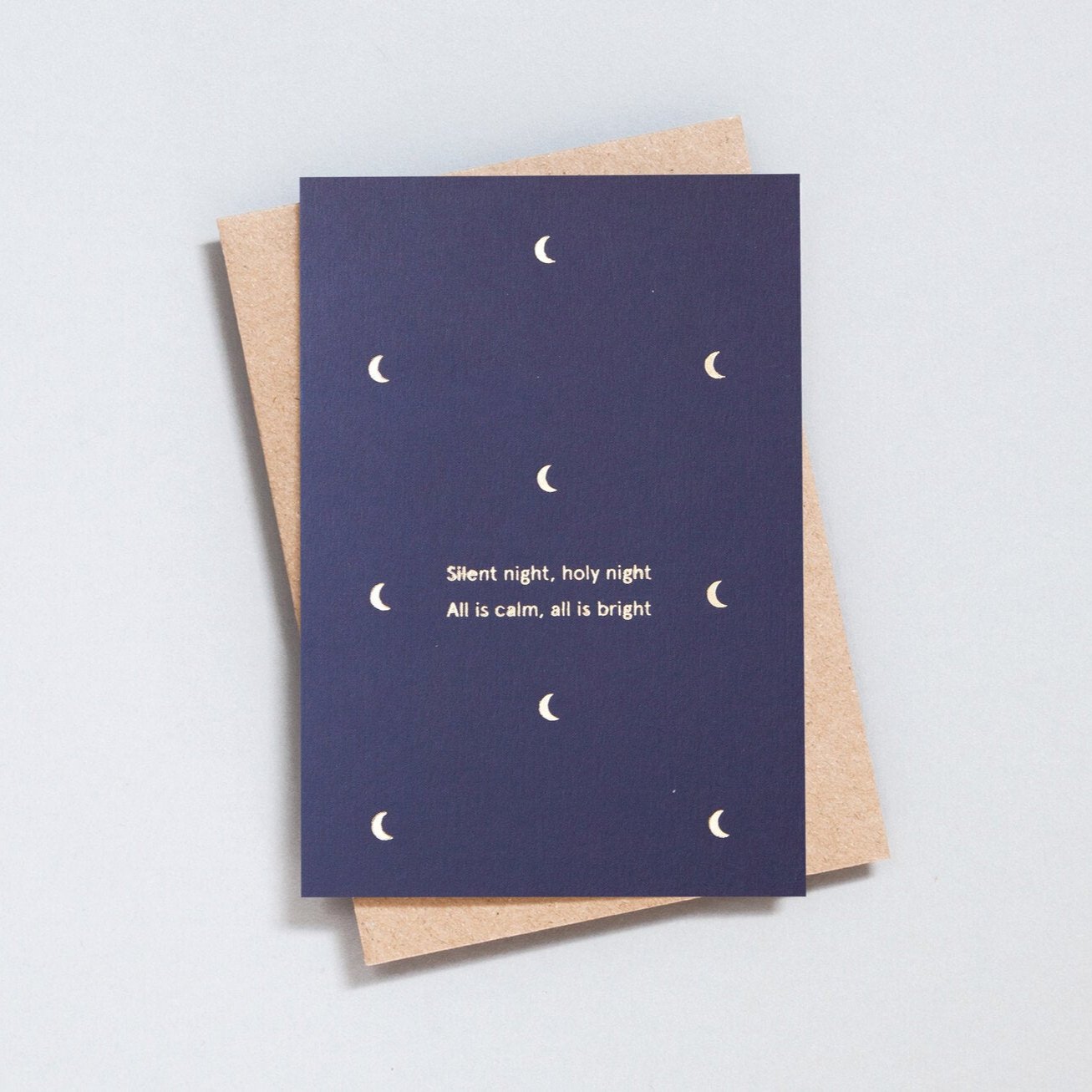 Navy blue Christmas card with small foil blocked moon motifs in brass, with the words 'Silent night, holy night, All is calm, all is bright'. With brown kraft envelope.