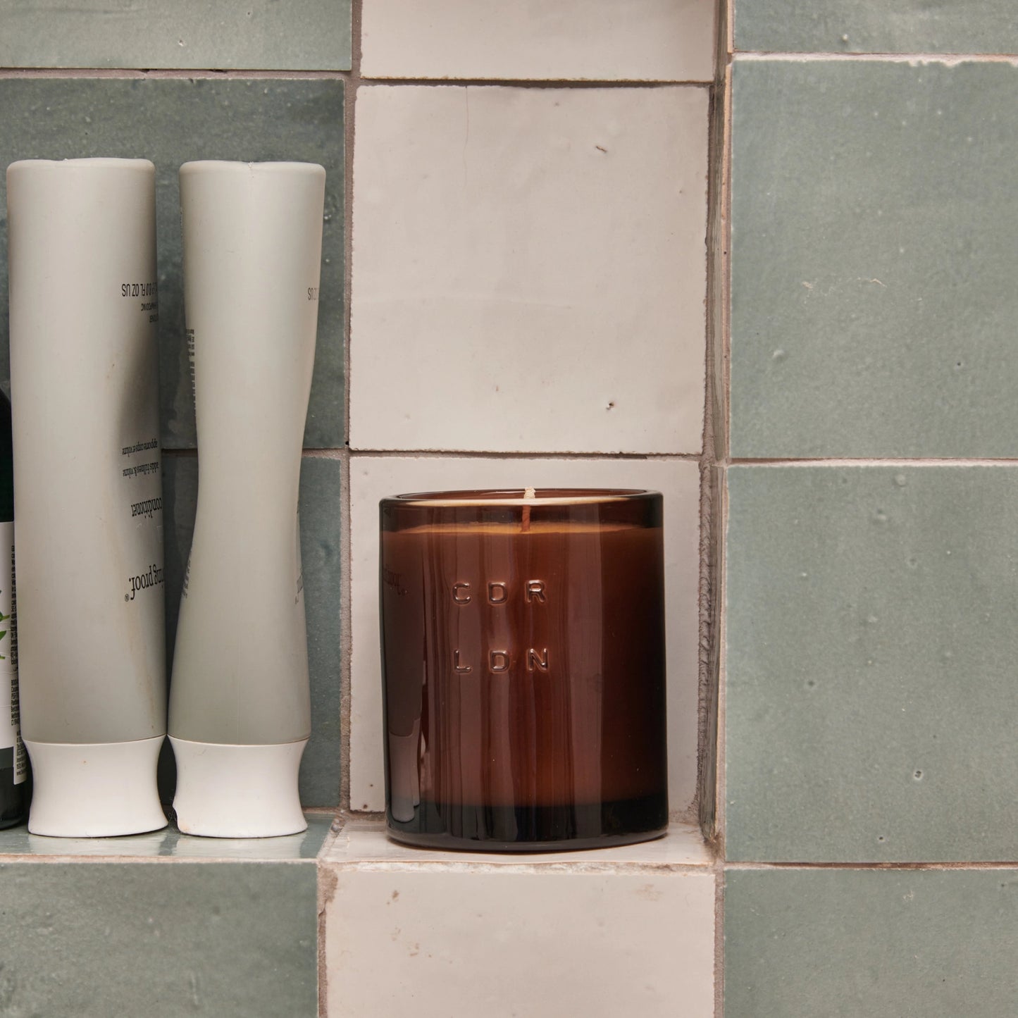 Brown candle with 'CDR LDN' branding on a tiled surface next to two white cylindrical objects.