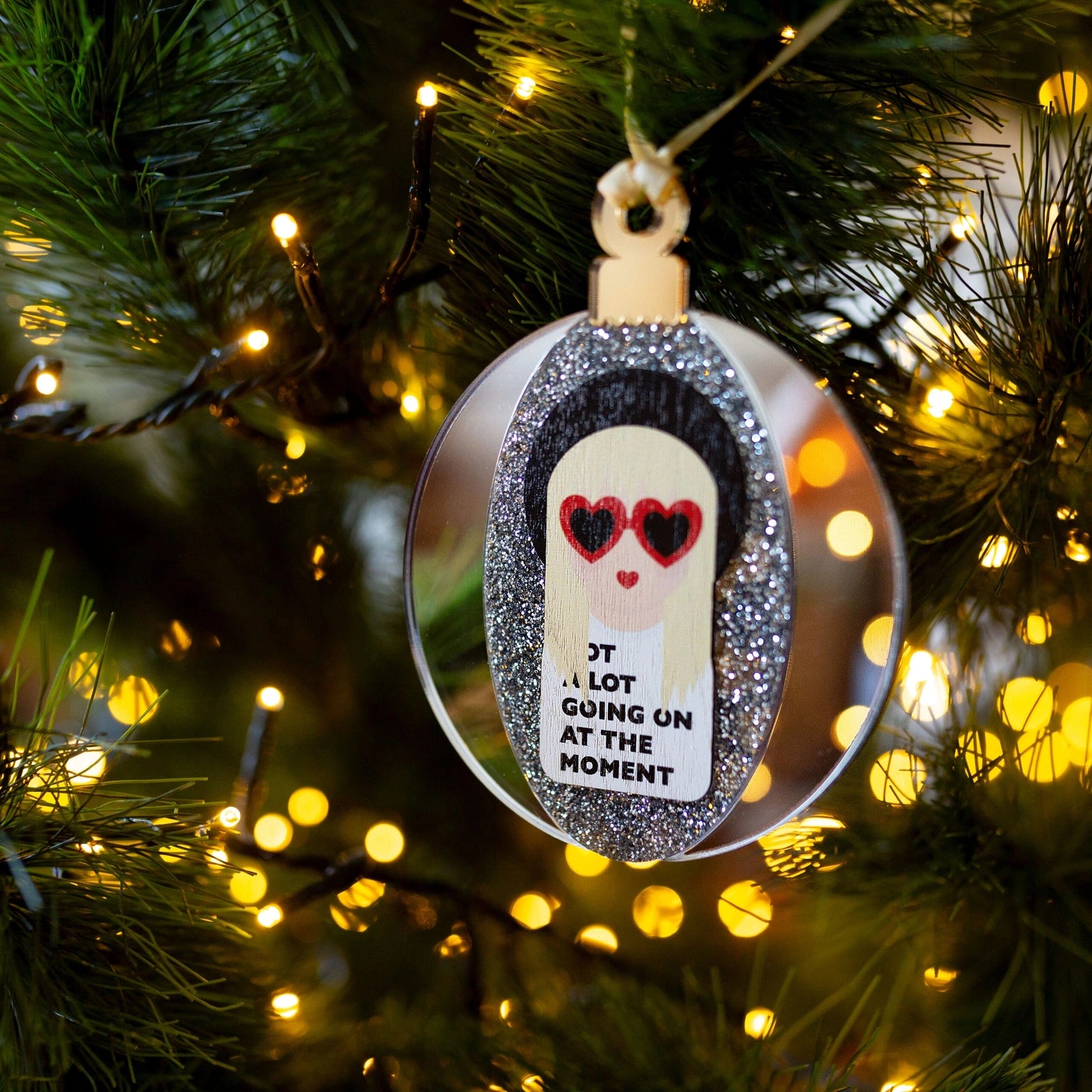 Mirrored silver Taylor Swift bauble hanging in a Christmas tree.