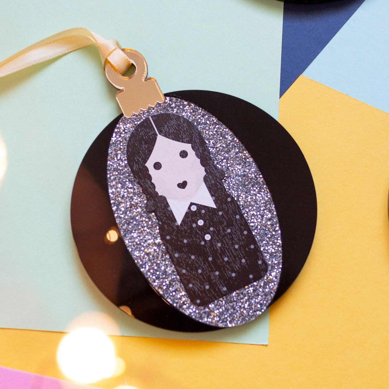 Black & silver Wednesday Addams bauble on a colourful background.