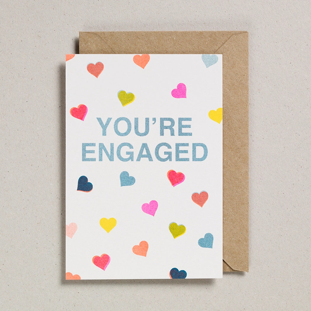 Card with 'You're Engaged' text and colorful hearts on a beige background